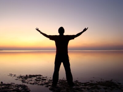 man with outstretched arms facing sunrise