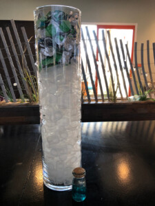 Tall glass vessel filled with recycled plastics