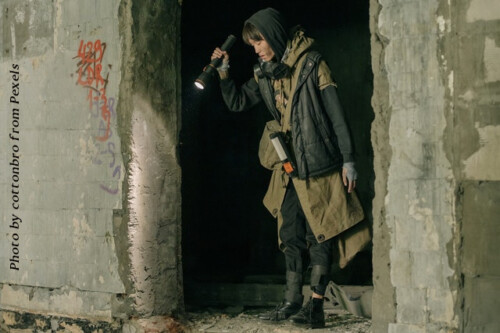woman wearing black and brown coat in concrete wall opening using flashlight