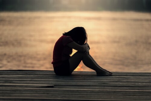 woman sitting on lake dock with head down and arms over knees