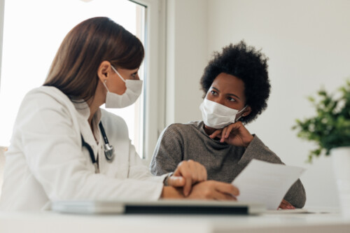 nurse talking with patient, both wearing masks