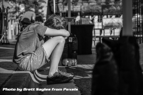 teen sitting on curb with head bowed on knees