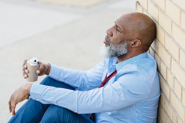 man sitting and leaning on brick wall with a beer can