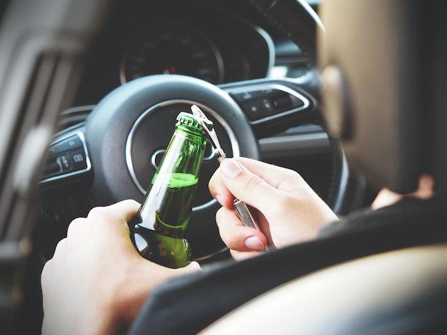 man opening beer bottle in car